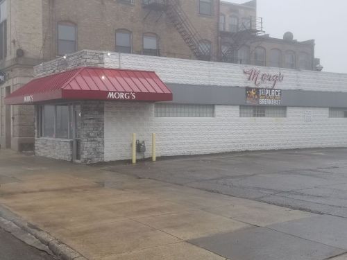 A foggy street view of Morg's restaurant with a red awning and a sign for breakfast.
