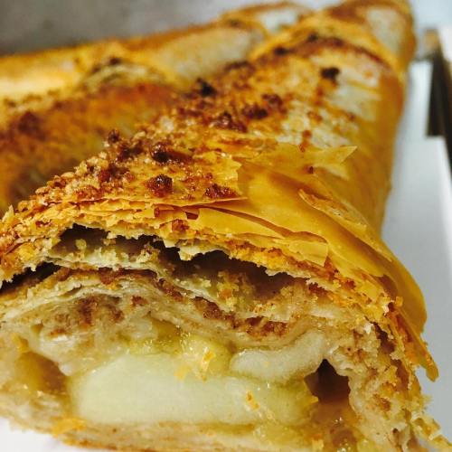 Close-up of a golden-brown pastry roll filled with apple, showcasing flaky layers and a crispy texture.