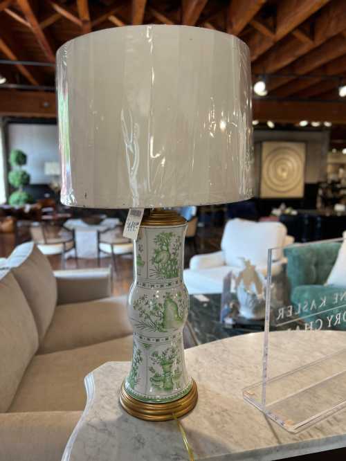 A decorative lamp with a green and white floral design and a white shade, placed on a marble surface in a stylish interior.