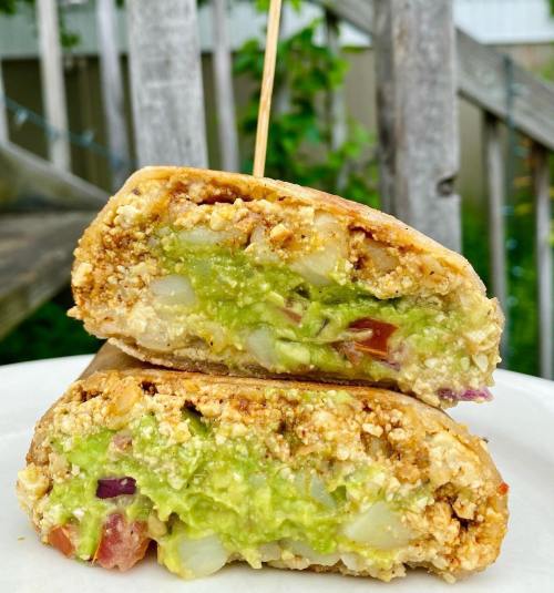 A close-up of a halved sandwich filled with green guacamole, diced vegetables, and a golden-brown crust on a plate.