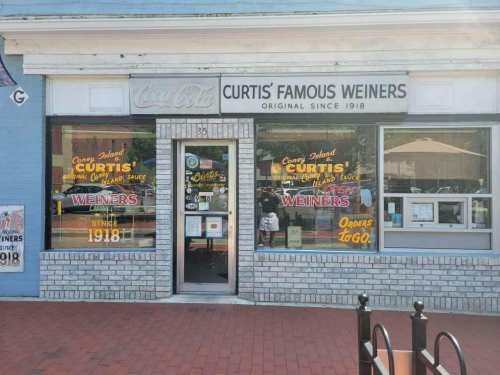 Exterior of Curtis' Famous Weiners, a colorful storefront with large windows and signage, established in 1918.