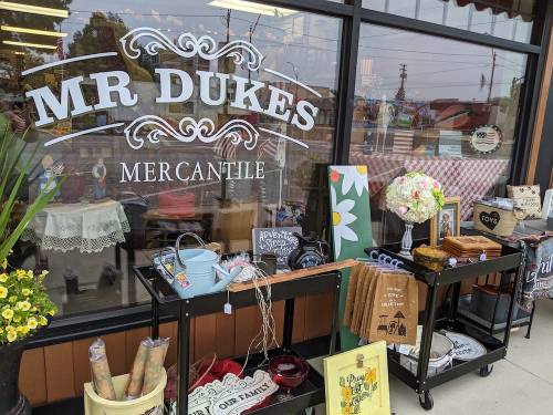 A storefront display of Mr. Dukes Mercantile featuring various decorative items and flowers outside.