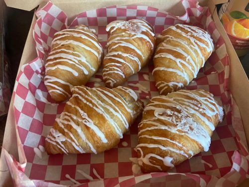 A box of five glazed croissants drizzled with white icing on a red and white checkered paper.