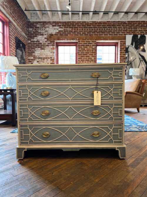 A stylish blue dresser with decorative trim and gold handles, set in a rustic room with brick walls and wooden floors.