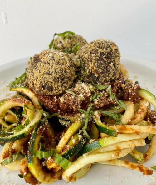 A plate of zucchini noodles topped with meatballs, marinara sauce, and fresh herbs, garnished with grated cheese.