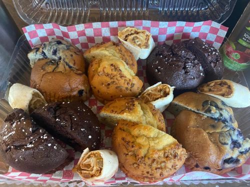 A variety of baked goods including muffins and pastries in a clear container with a red checkered liner.