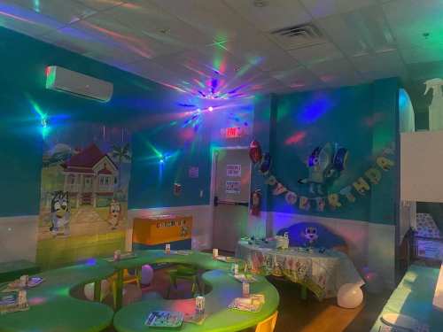 A colorful party room with a decorated table, vibrant lights, and a birthday banner on the wall.