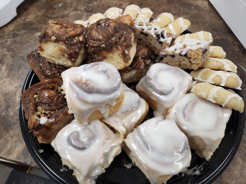 A black plate filled with assorted pastries, including cinnamon rolls and iced cookies, arranged attractively.