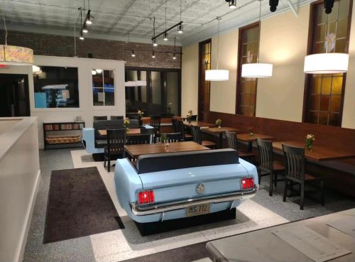 A retro diner interior featuring blue car seating, wooden tables, and modern lighting.