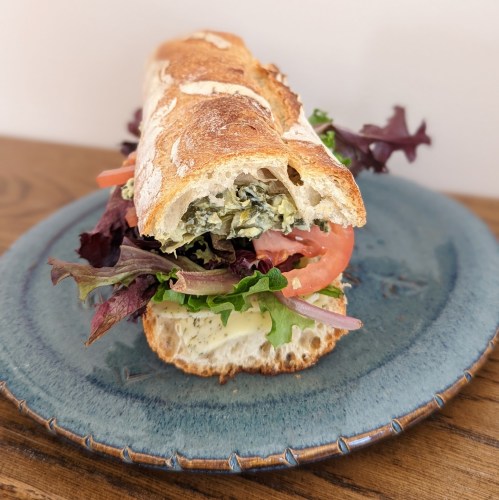 A fresh sandwich on a blue plate, filled with greens, tomato, and a creamy spread, served on crusty bread.