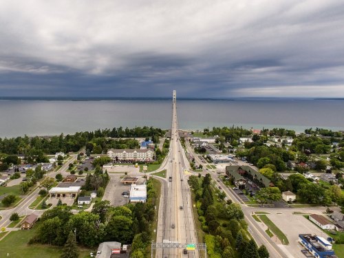 Aerial view of a long bridge connecting land to the horizon, with dark clouds above and a calm body of water below.