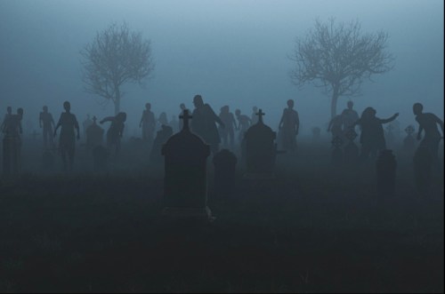 Silhouettes of figures in a foggy graveyard, surrounded by tombstones and bare trees.