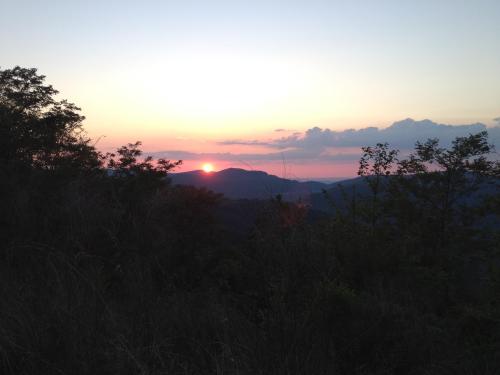 Sunset over a mountainous landscape, with silhouettes of trees in the foreground and a colorful sky.
