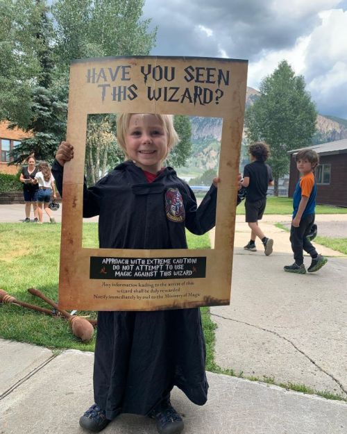 A child in a wizard costume holds a sign that reads, "Have you seen this wizard?" against a scenic background.