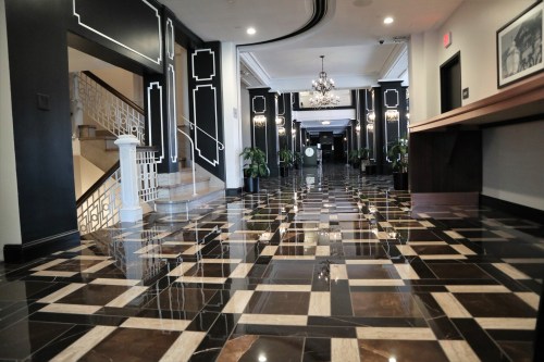 Elegant hotel lobby with polished black and white tiled floor, stylish decor, and a grand staircase.