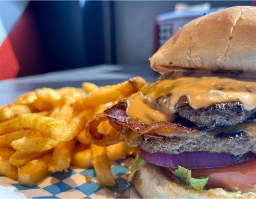 A close-up of a juicy burger with bacon, cheese, lettuce, and tomato, served with a side of curly fries.