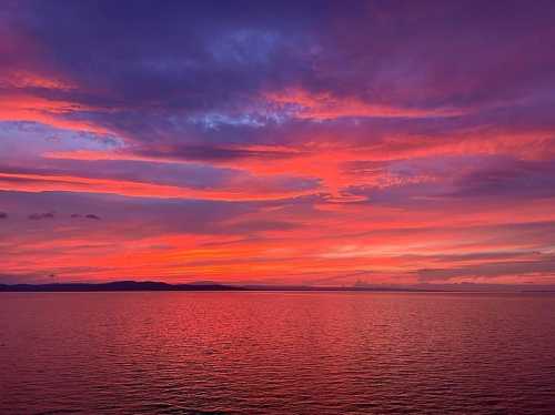 A vibrant sunset over calm waters, with shades of pink, purple, and orange reflecting on the surface.