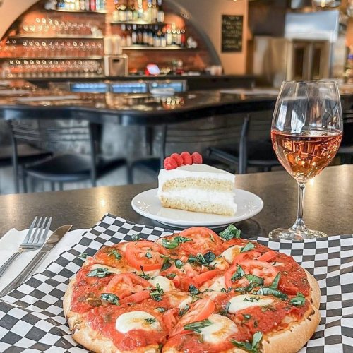 A delicious pizza topped with tomatoes and herbs, served with a glass of rosé wine and a slice of cake in a restaurant.
