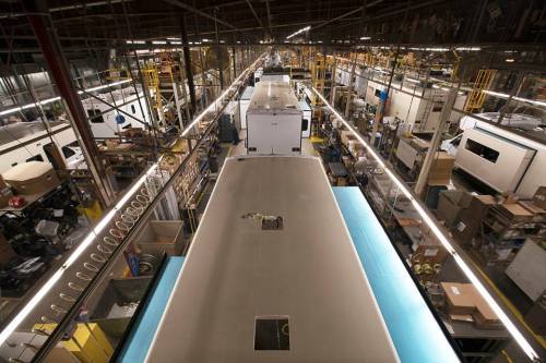 Aerial view of a factory floor with multiple RVs in production, surrounded by equipment and materials.