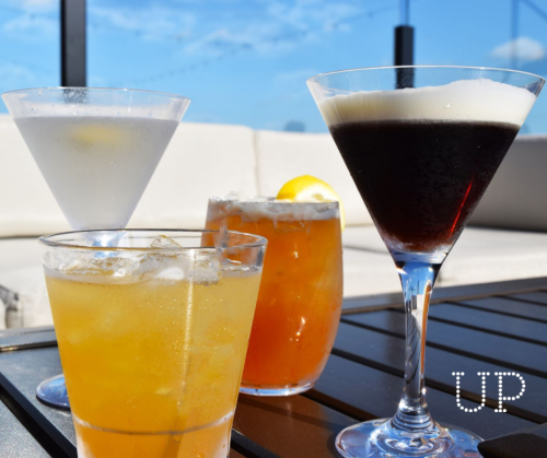 Four colorful cocktails on a table, with a clear blue sky in the background.
