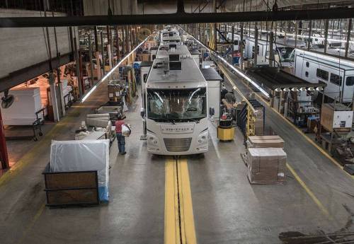 A spacious manufacturing facility with several RVs in production, workers are seen along the assembly line.