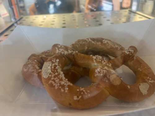 A close-up of three soft pretzels sprinkled with coarse salt, displayed in a clear container.