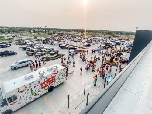 Aerial view of a busy parking lot with a food truck and a crowd of people gathered for an event during sunset.