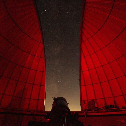 A telescope inside a red-lit observatory, with a starry sky visible through the opening.
