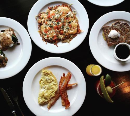 A table set with four plates of breakfast dishes, including an omelet, hash browns, French toast, and a drink.