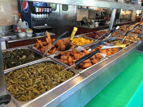A buffet table featuring various dishes, including fried chicken, greens, and assorted sides in metal trays.