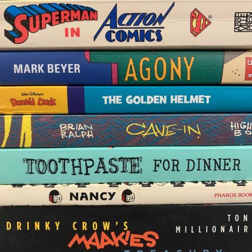A stack of comic books and graphic novels with colorful covers, including titles like "Superman," "Agony," and "Toothpaste for Dinner."