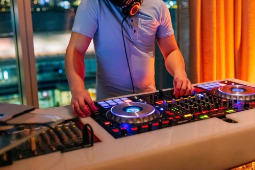 A DJ mixes music at a vibrant event, using a colorful DJ controller with city lights in the background.