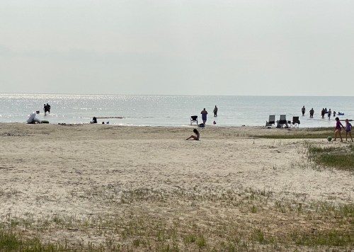 A sandy beach with people walking and relaxing by the water, with a few chairs set up in the background.