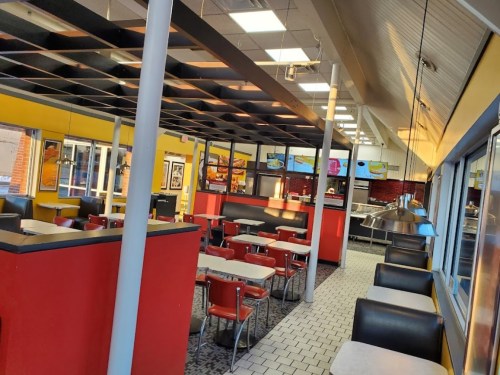 Interior of a diner featuring red and black decor, tables, chairs, and a counter with food displays.