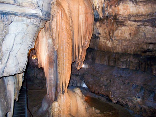 Stalactites and stalagmites in a dimly lit cave, with water pooling on the ground and rocky walls.
