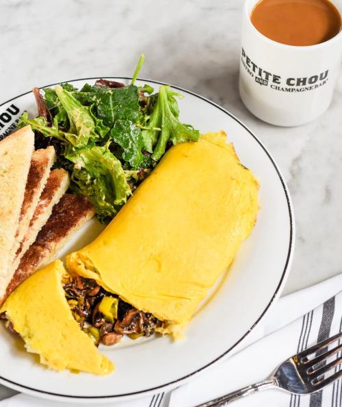 A fluffy omelette filled with vegetables, served with toast, a side salad, and a cup of coffee on a marble table.
