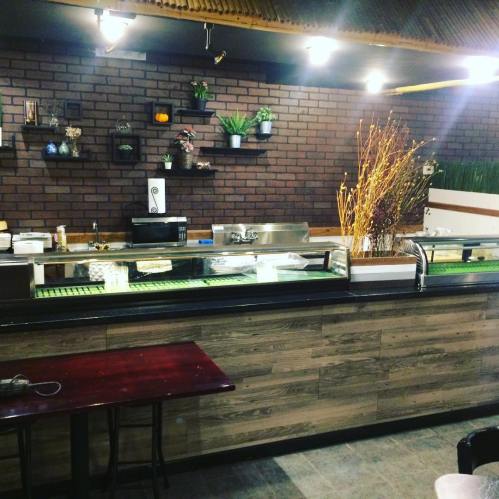 A cozy restaurant interior featuring a wooden counter, plants on the wall, and a display of sushi or food items.