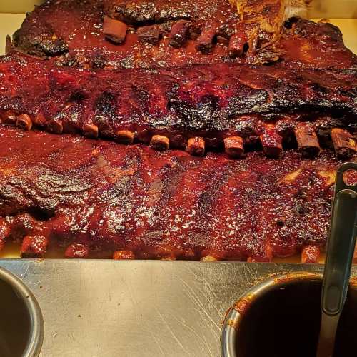 Close-up of glazed barbecue ribs on a platter, with two small bowls of sauce beside them.