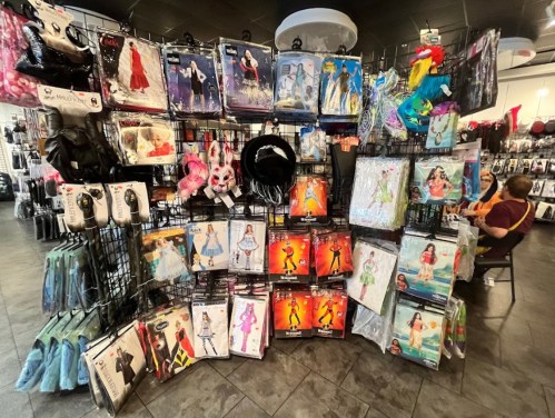 A display of various costumes and accessories hanging on racks in a store, with a person seated in the background.