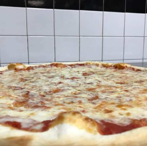 A close-up of a cheese pizza with a golden crust, set against a tiled wall.