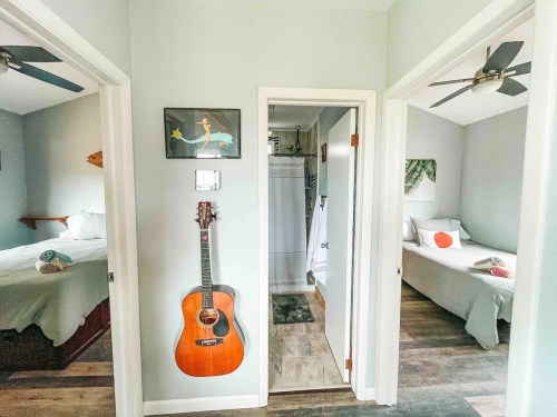 A light-colored hallway with two open doorways leading to bedrooms, featuring a guitar on the wall and ceiling fans.