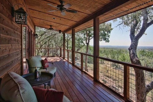 A wooden porch with comfortable seating, overlooking a scenic view of trees and hills under a clear blue sky.