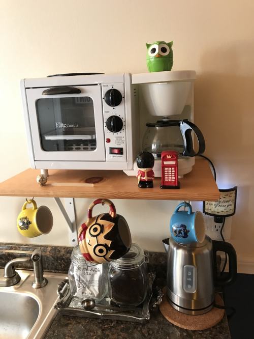 A kitchen counter with a microwave, coffee maker, kettle, and colorful mugs, including a Harry Potter mug and an owl.