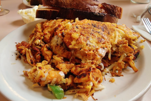 A plate of crispy hash browns mixed with vegetables, served with slices of toasted bread in the background.