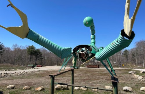 A large, whimsical sculpture of a lobster made from metal and pipes, set against a clear blue sky.