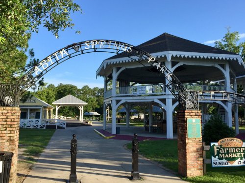 Archway reading "Abita Springs Park" leading to a gazebo in a green park setting with clear blue skies.