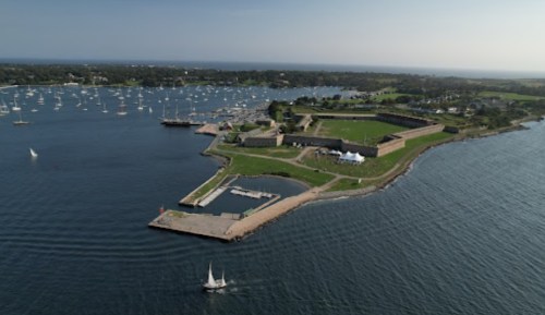 Aerial view of a coastal area with a fort, green fields, and sailboats in the water.
