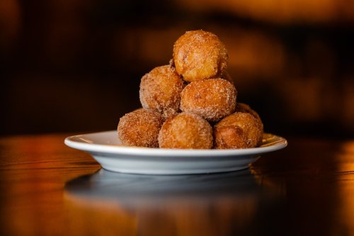 A plate of golden, sugar-coated doughnut holes stacked in a pyramid shape.