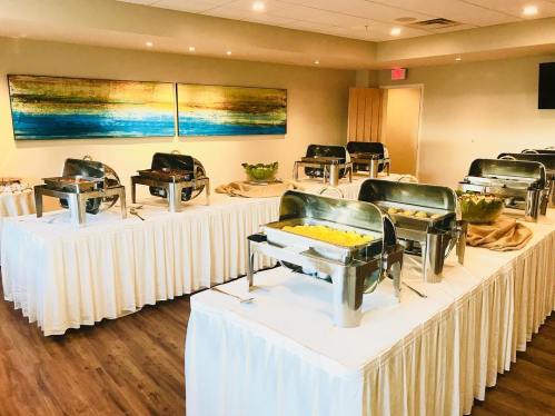 A spacious buffet setup with multiple chafing dishes on tables, decorated with tablecloths and fresh greenery.