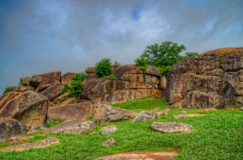 A rocky landscape with large boulders and green grass under a cloudy sky.
